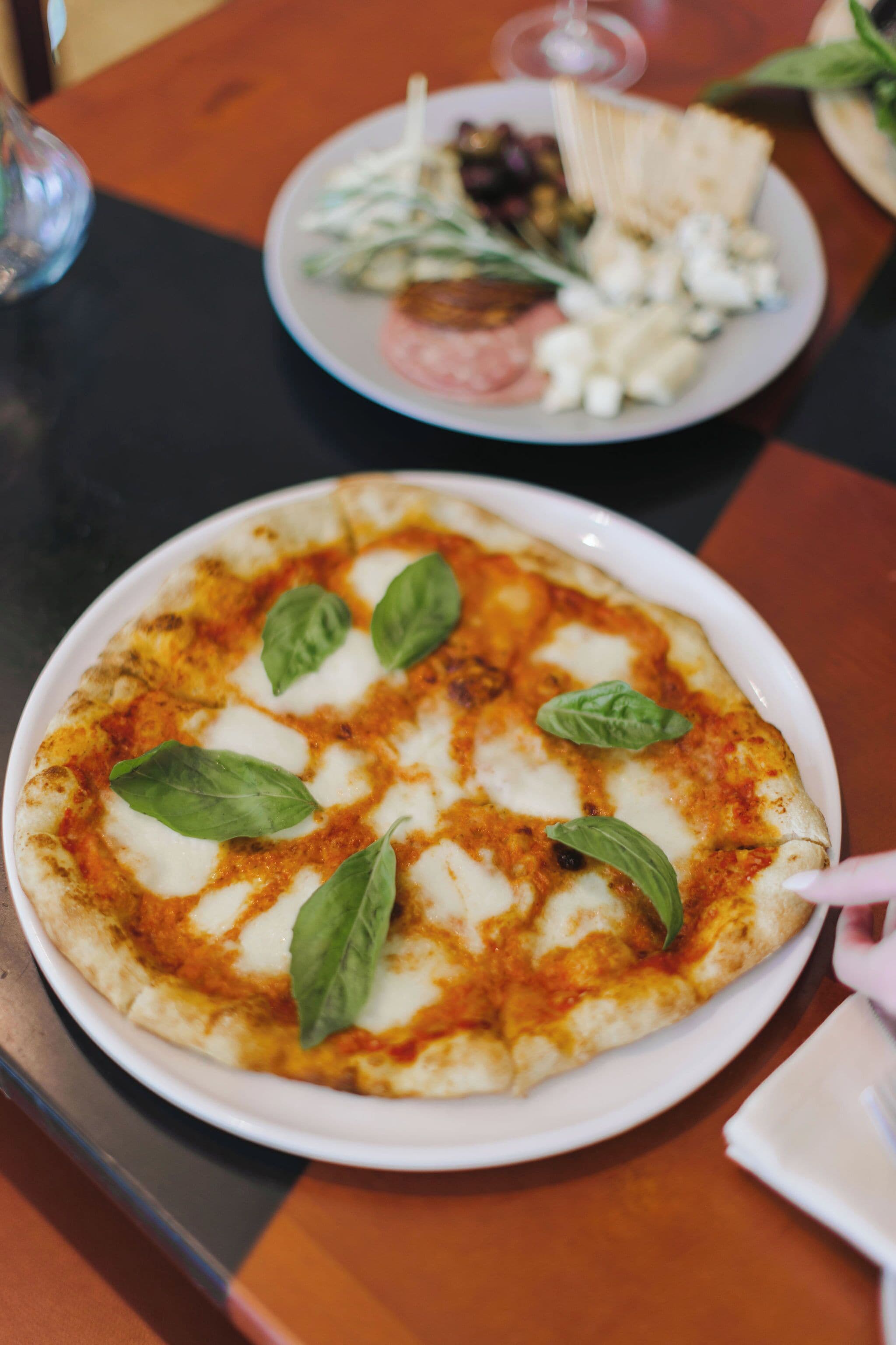Una pizza con hojas de albahaca sobre un plato blanco.