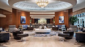 A spacious lobby with a central seating area, a bar in the background, and large windows providing natural light.