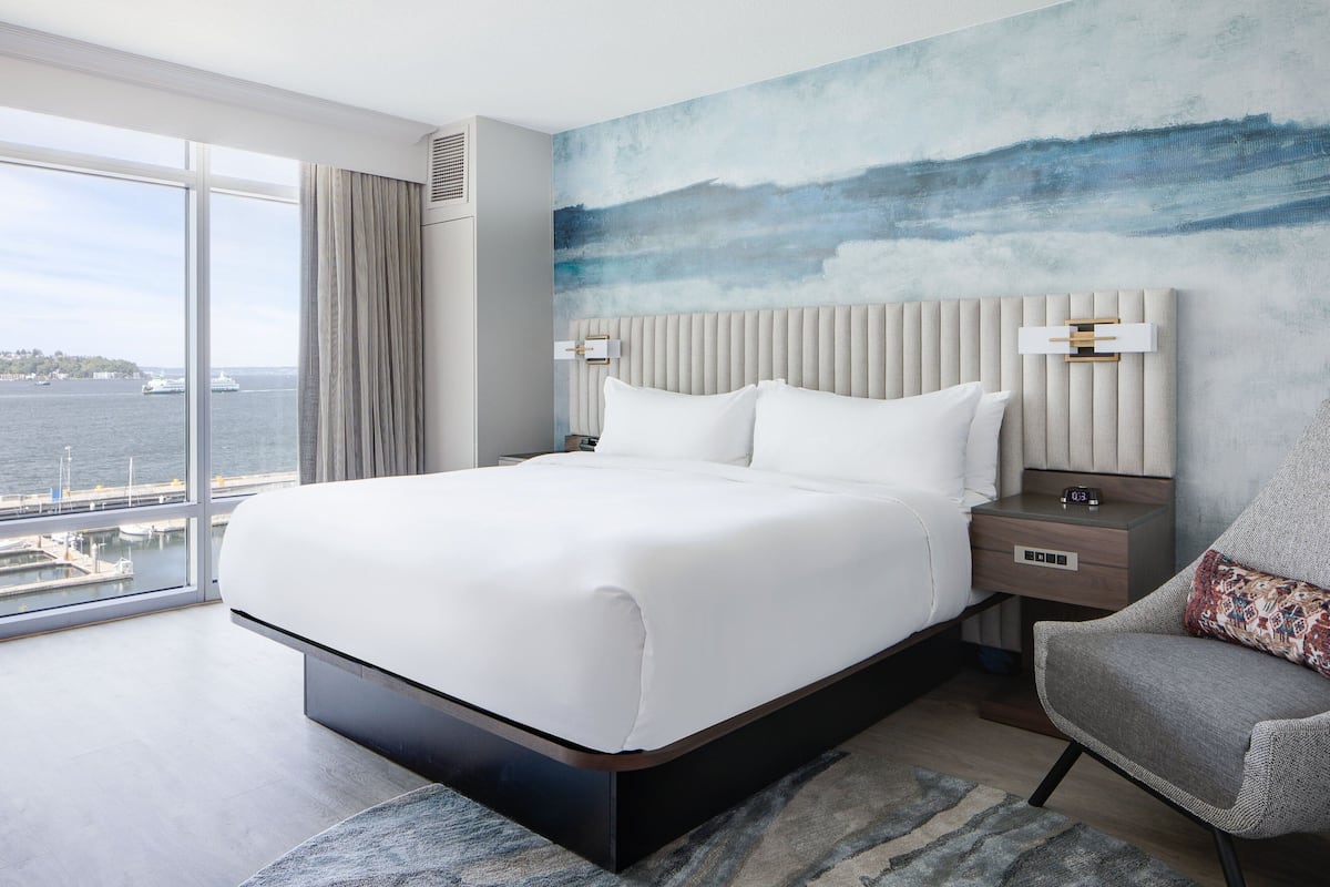 A modern hotel room with a large bed, a view of the water, and a cityscape.