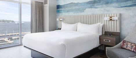 Una moderna camera d'albergo con un letto grande, vista sull'acqua e sullo skyline della città.