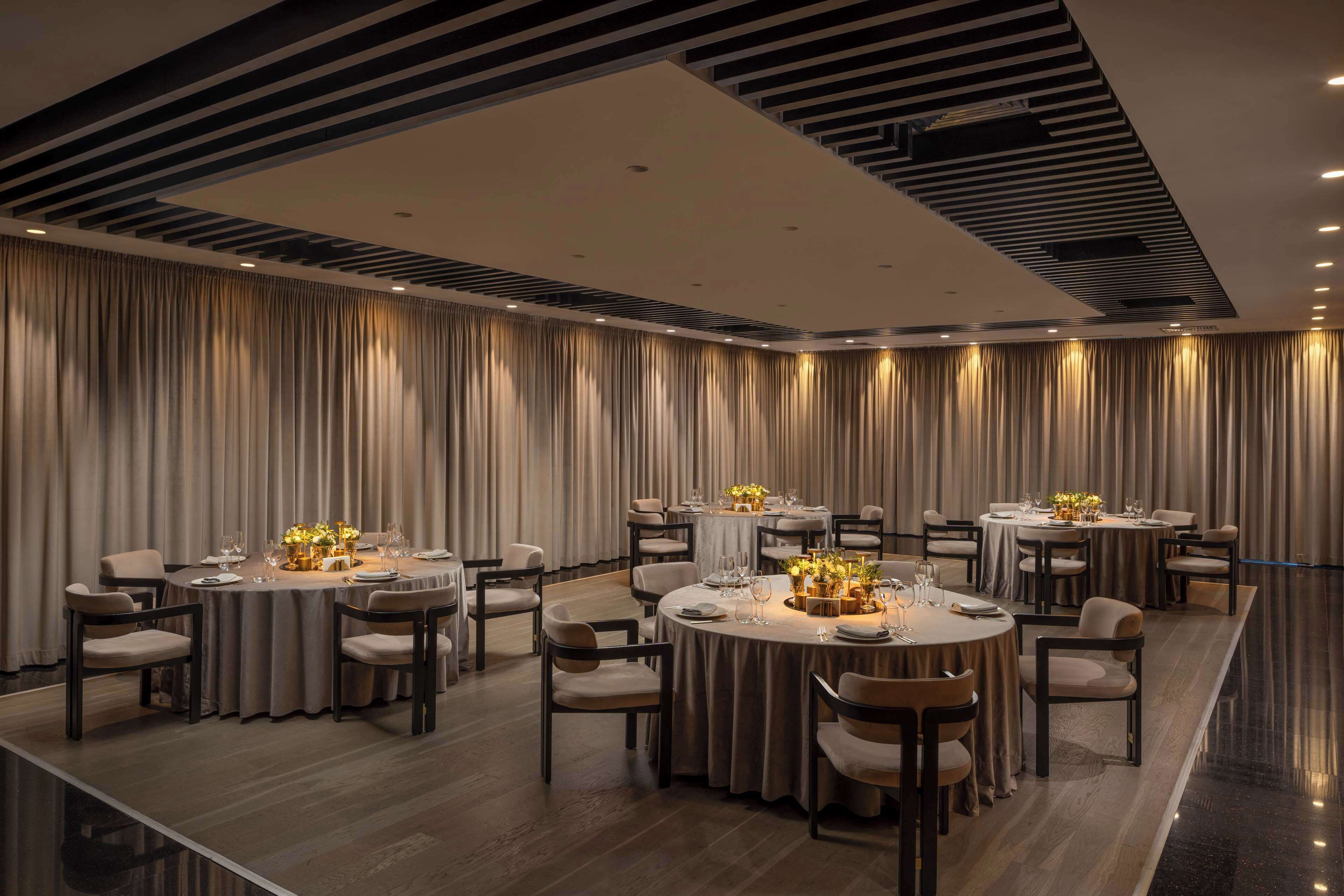 A modern dining room with round tables, chairs, and a long table with a floral centerpiece.