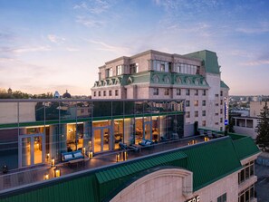 A hotel with a glass facade, outdoor seating area, and a green roof. - Radisson Blu Leogrand Hotel (Chisinau)