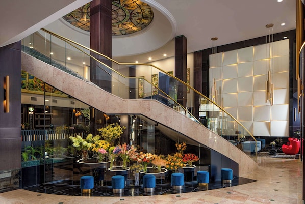 Un vestíbulo moderno con una escalera curva, barandillas de vidrio y un arreglo floral central.