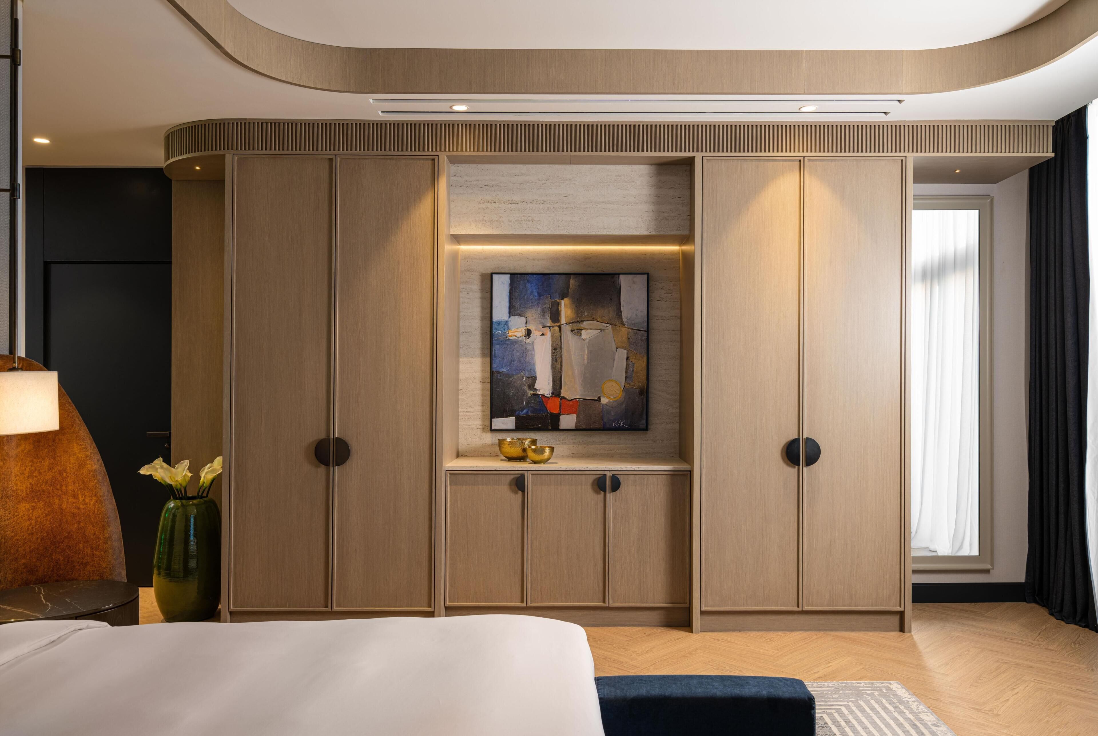 A hotel room with a bed, a large artwork on the wall, and a view of the outdoors.