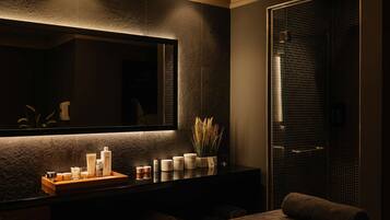 A modern spa room with a massage table, a large mirror, and a wall-mounted shelf with toiletries.