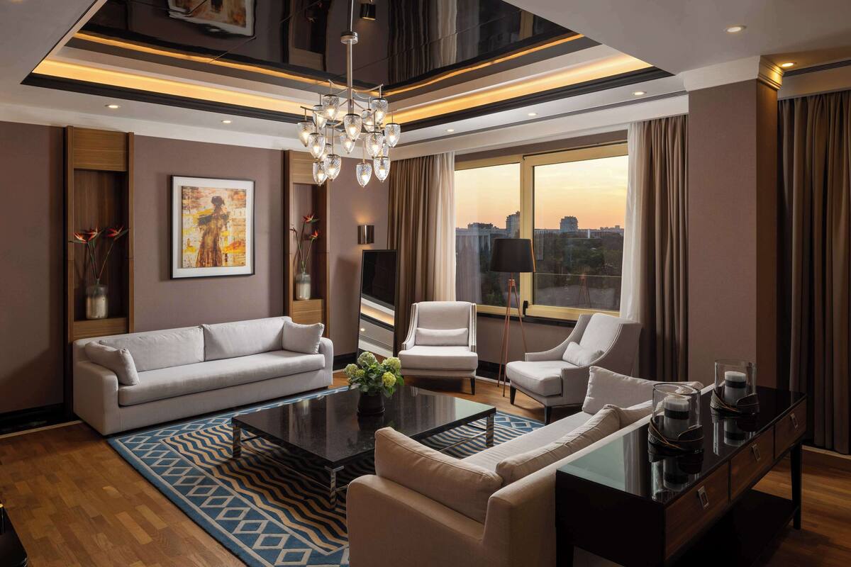 A modern living room with a sofa, armchairs, a coffee table, and a city view through large windows.