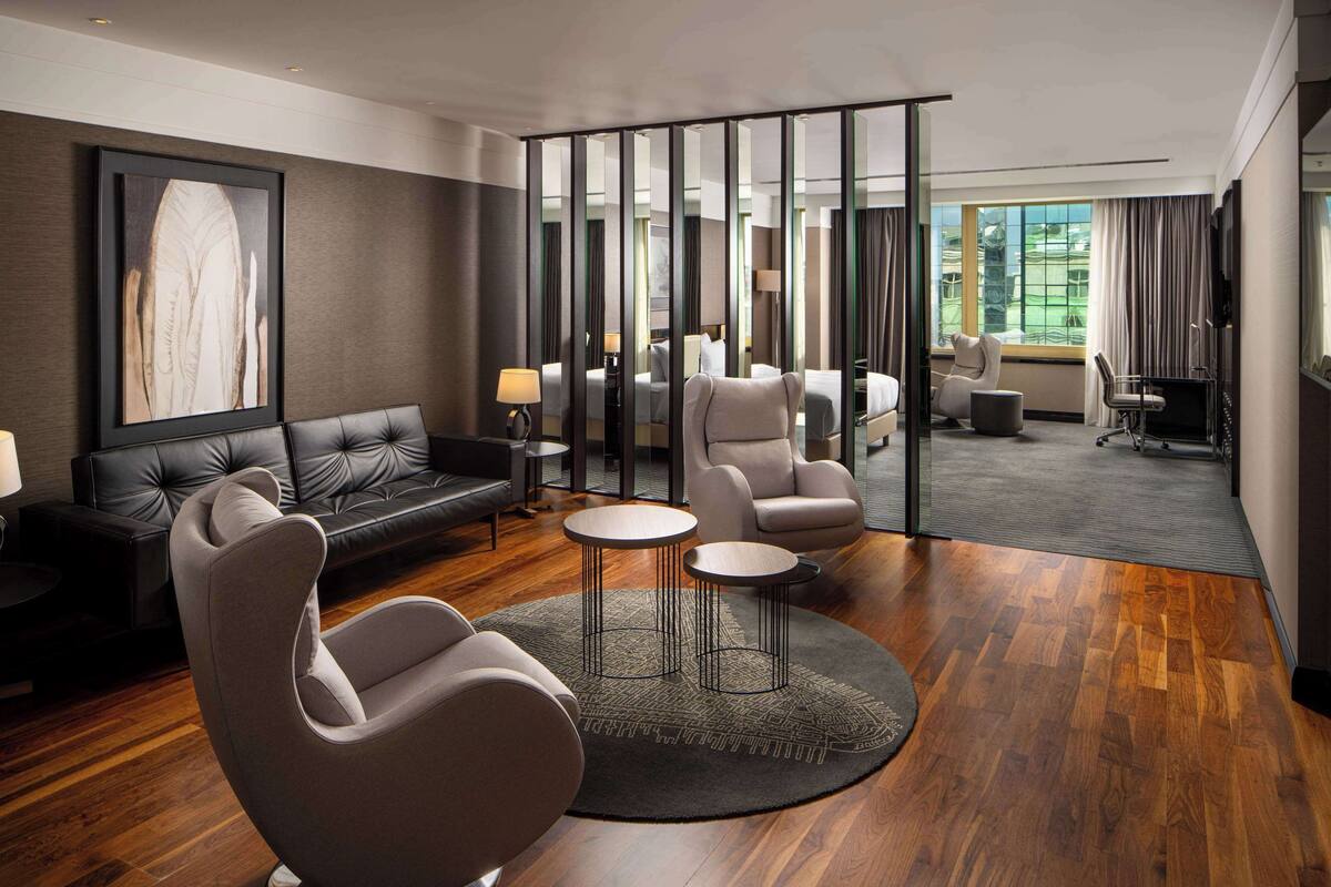 A modern hotel room with a leather sofa, two armchairs, a round coffee table, and a large mirror.