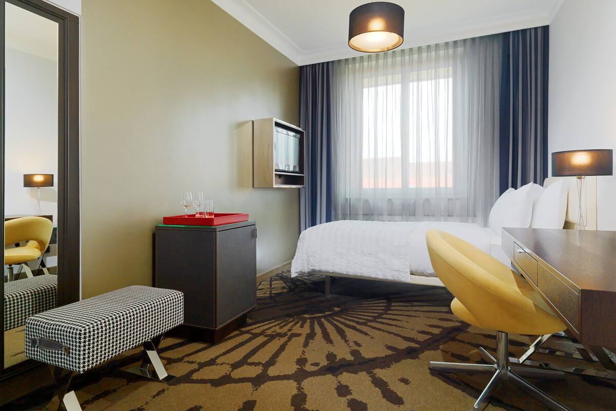 Une chambre d’hôtel équipée d’un lit, d’un bureau, d’une chaise, d’une télévision et d’un miroir.