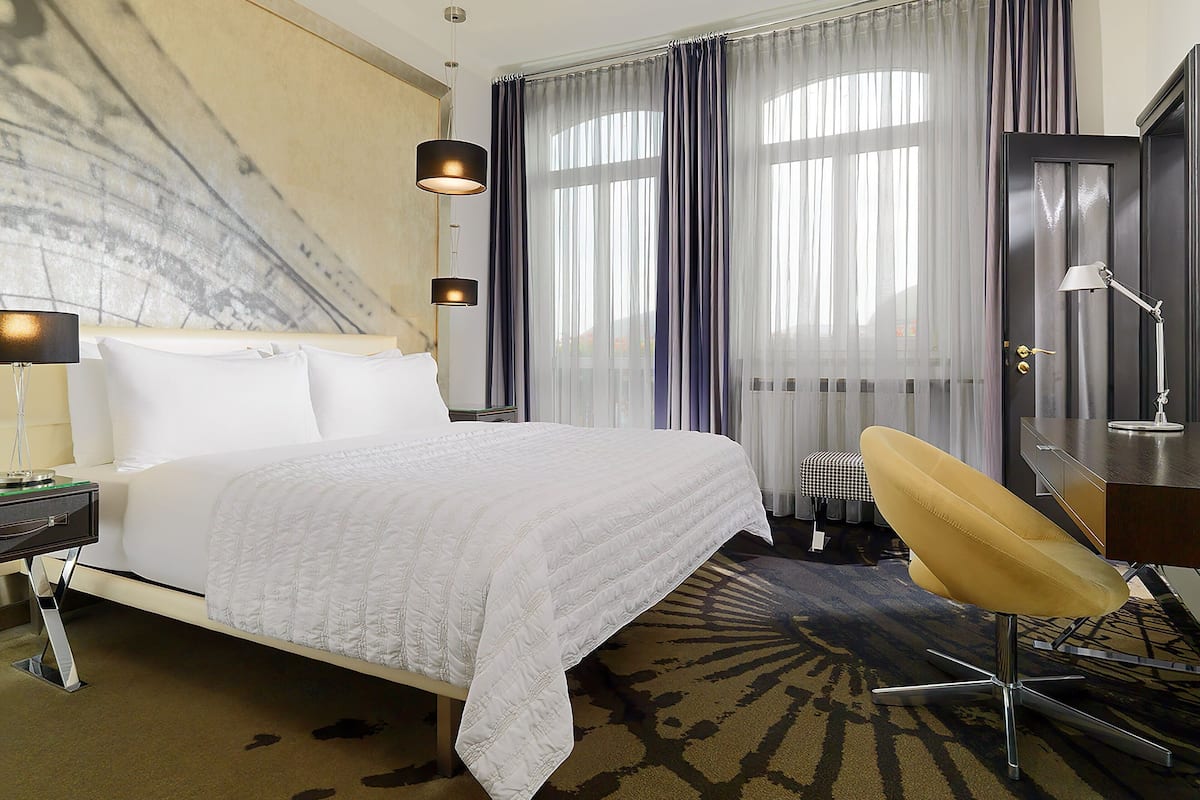 Une chambre d’hôtel avec un lit, un bureau, une chaise et une grande fenêtre avec des rideaux.