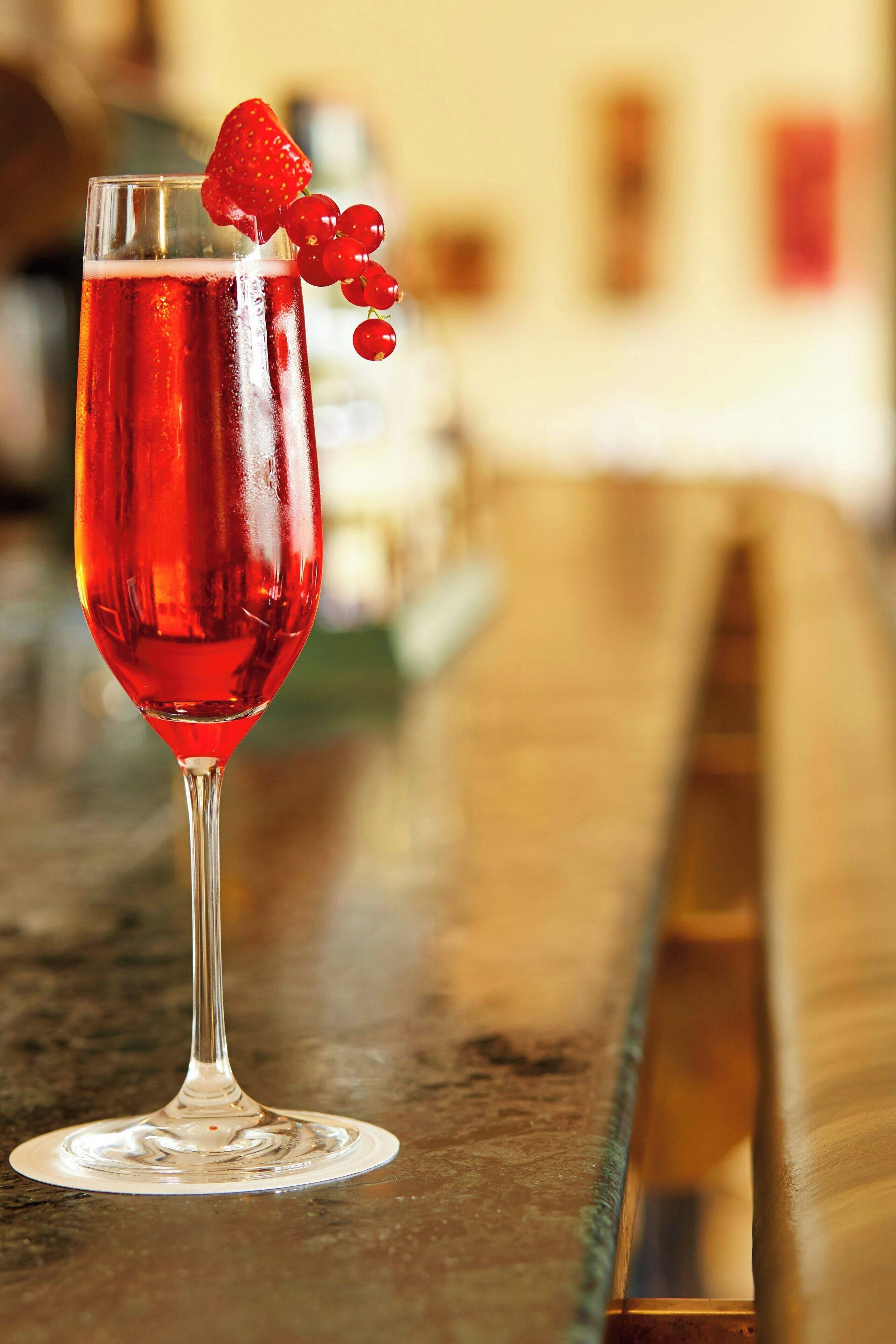 A glass of red beverage with a strawberry and red berries on the rim, placed on a bar counter.