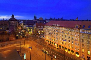 A grand hotel with multiple floors, a prominent entrance, and a large building with a red roof in the background.