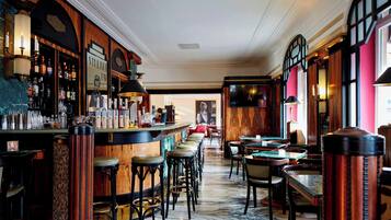 A bar area with a marble floor, wooden bar counter, and stools. There are tables and chairs in the background.