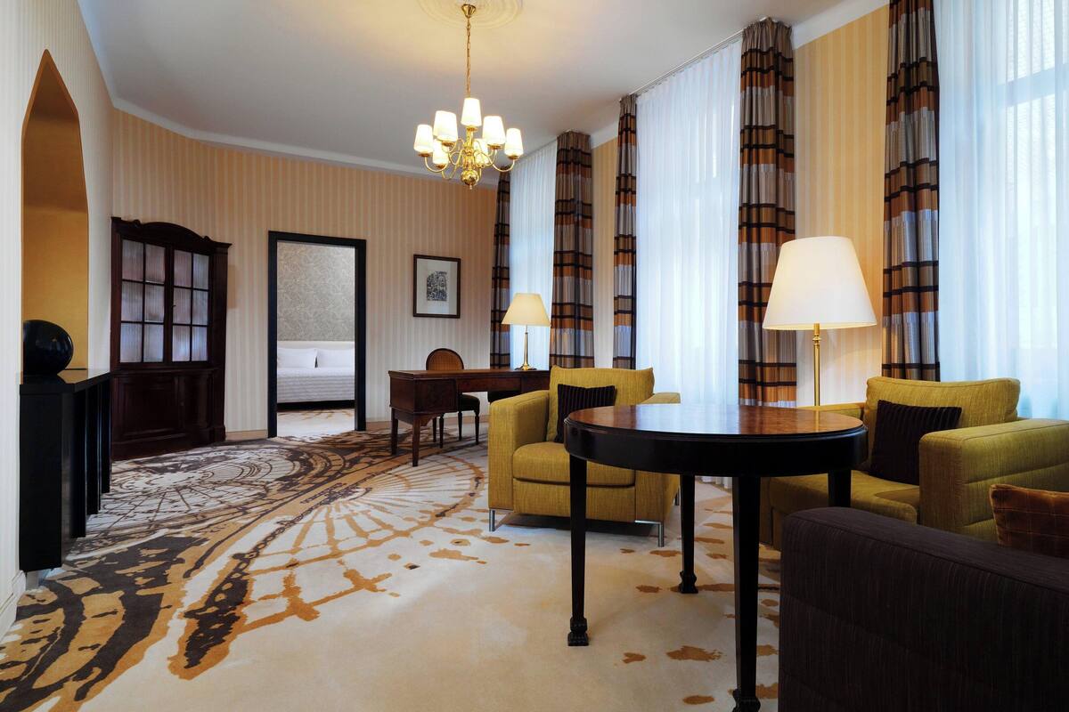 Une chambre d’hôtel dotée d’un grand tapis à motifs, d’un lustre et d’un ensemble de meubles de salon.