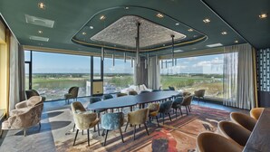 A conference room with a large table and chairs, large windows with a view of a landscape, and a modern ceiling design.