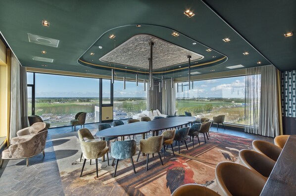 A conference room with a large table and chairs, large windows with a view of a landscape, and a modern ceiling design.