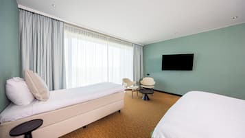 Una habitación de hotel con cama, una silla, una mesita, televisor y un ventanal con cortinas.