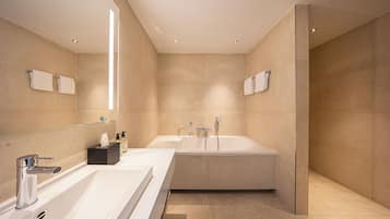 Une salle de bain moderne dotée d’une grande baignoire, de deux lavabos et d’une douche à parois de verre.