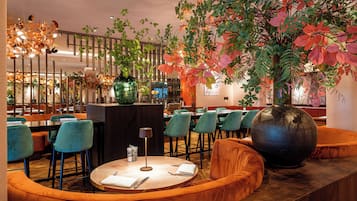 A restaurant with a round table, chairs, and a large vase with plants.