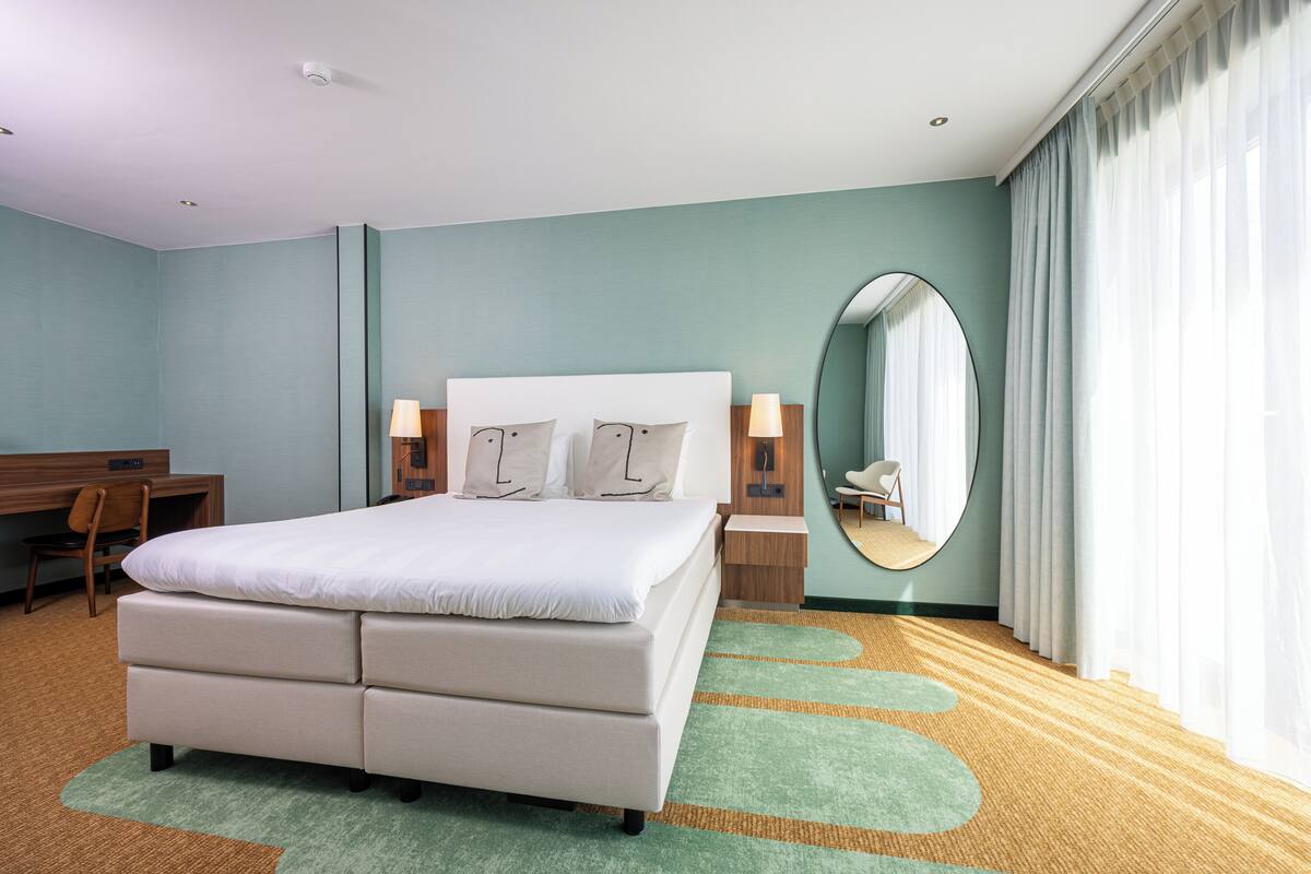 Una camera d'albergo con un letto, una scrivania, una sedia, uno specchio e vista sull'esterno.
