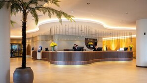 A modern reception desk with a curved design, a large potted palm tree, and a well-lit interior.