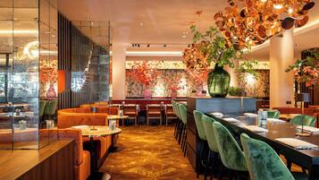 A restaurant with a modern interior, featuring a long dining table, cushioned seating, and decorative plants.