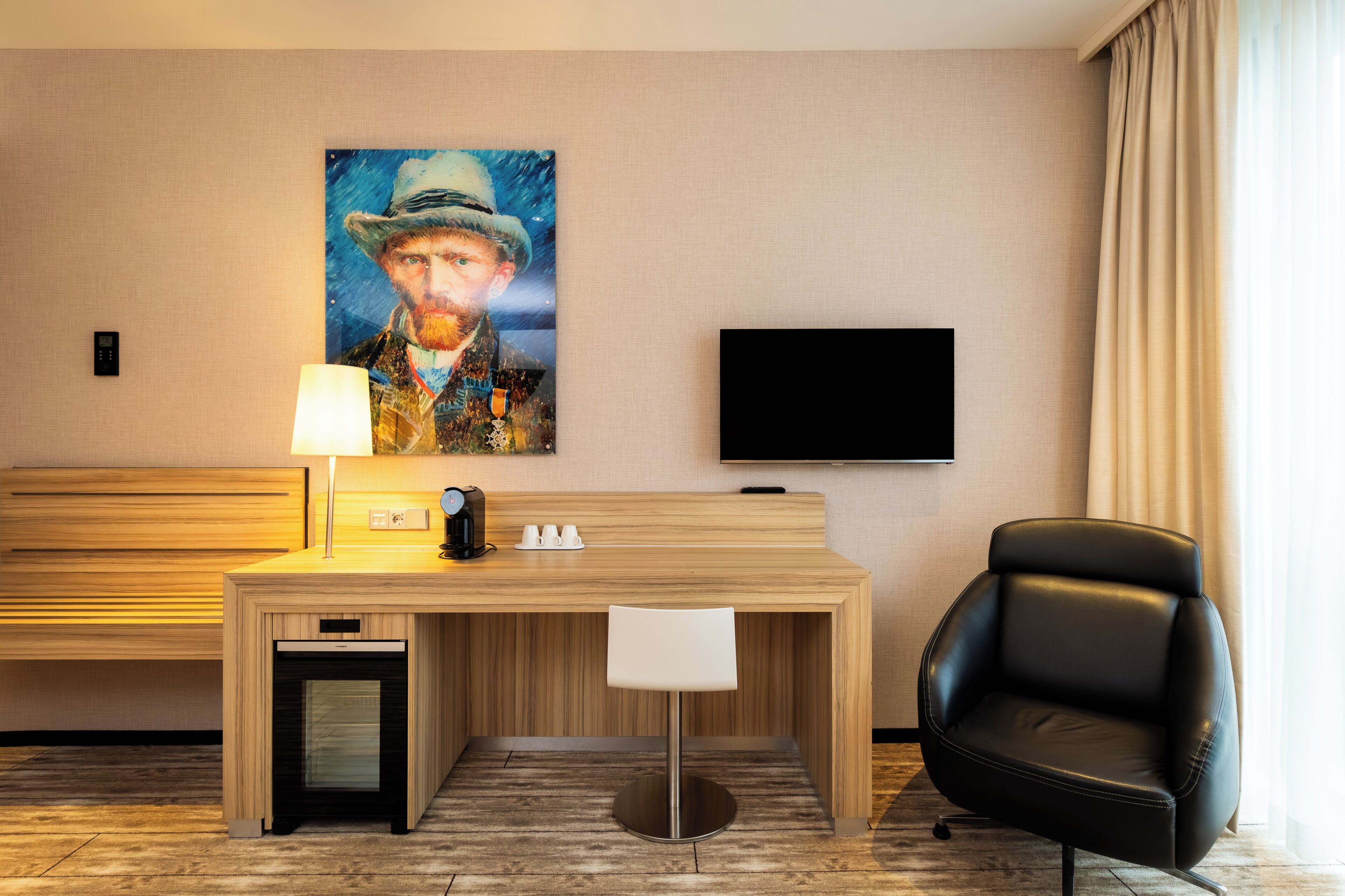 A hotel room with a wooden desk, a chair, a television, and a painting on the wall.