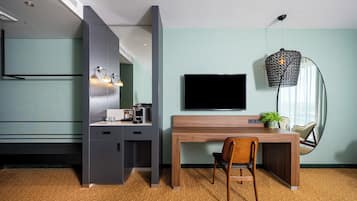 A modern hotel room with a wooden desk, a flat-screen TV, a sofa, and a large window.