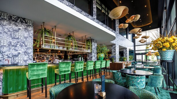 A modern bar area with green bar stools, a black round table, and a variety of seating options including patterned chairs and round tables.