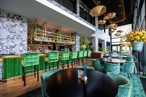 A modern bar area with green bar stools, a black round table, and a variety of seating options including patterned chairs and round tables. - Van der Valk Hotel Schiphol (Hoofddorp)