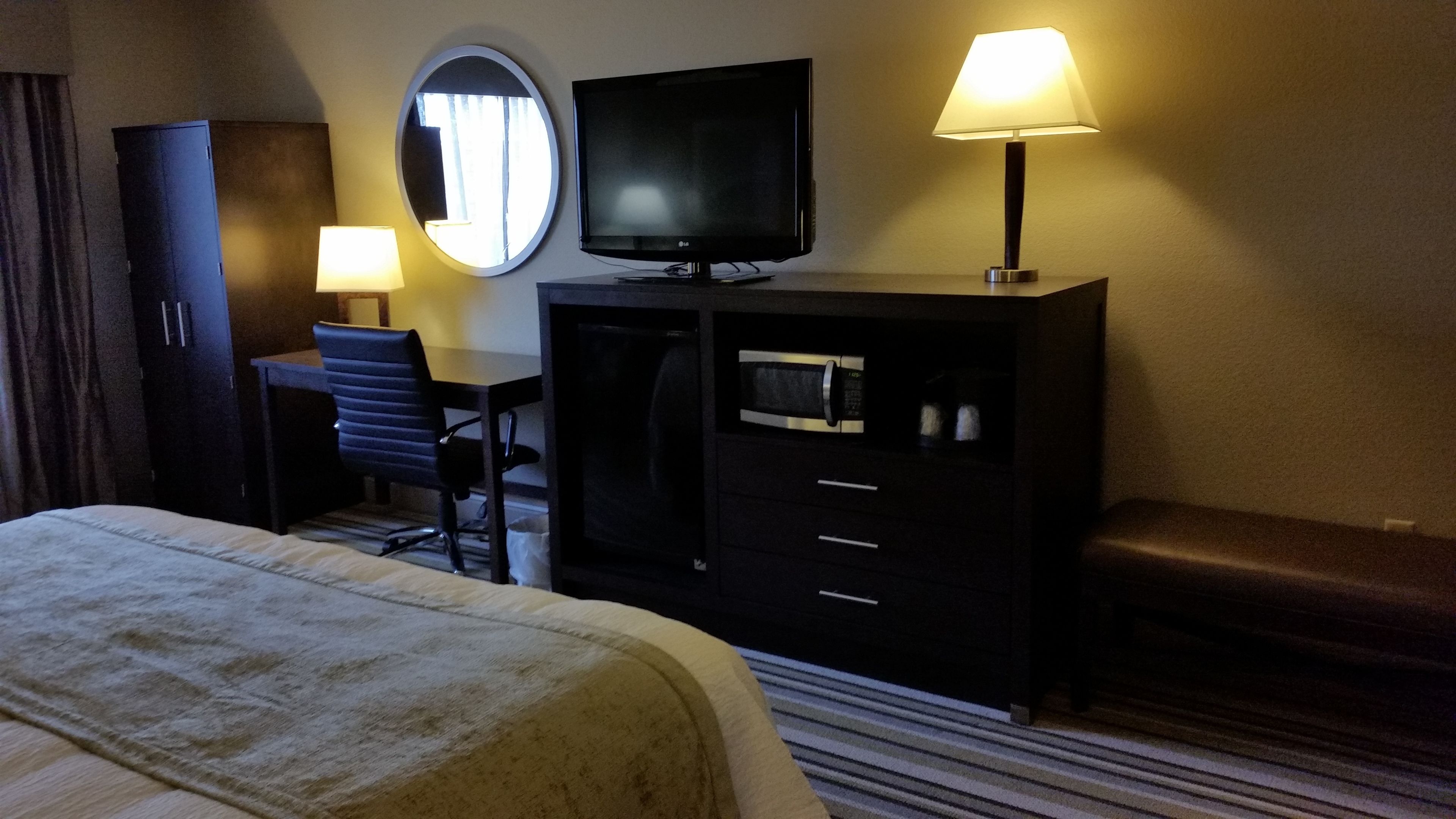 Una habitación de hotel con cama, escritorio, televisor, espejo, armario y lámpara.
