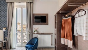 Una habitación de hotel moderna con un ventanal grande, un televisor de pantalla plana, una silla azul, un armario de madera y un radiador.