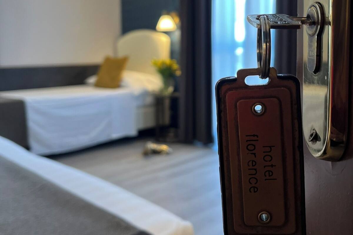 Camera d'albergo con un letto, un comodino, una lampada e vista sull'esterno attraverso una finestra.