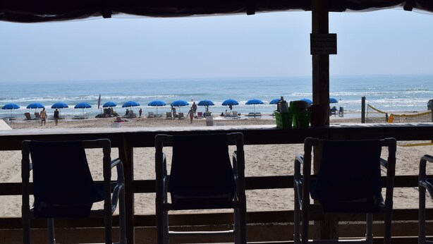 A beach view from a covered area with several chairs and umbrellas. - Wanna Wanna Inn (South Padre Island)
