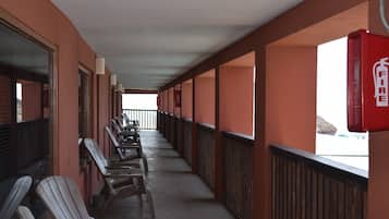 Un pasillo cubierto con filas de sillas de madera, un extintor fijado en la pared y vista a la playa por el extremo abierto.