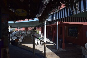 Un espacio de comedor al aire libre con mesas y sillas, una terraza de madera y un toldo a rayas.