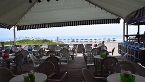 An outdoor seating area with tables and chairs, overlooking a beach with umbrellas. - Wanna Wanna Inn (South Padre Island)
