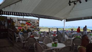 Un espacio al aire libre con mesas y sillas, una terraza de madera y vistas a la playa.