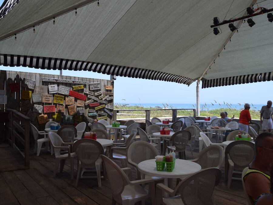 Un espacio al aire libre con mesas y sillas, una terraza de madera y vistas a la playa.