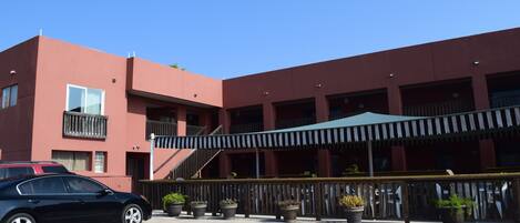 A multi-story building with a red facade, a covered outdoor seating area, and a car parked in front.
