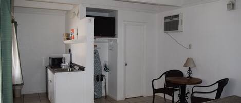 Ein kompaktes Hotelzimmer mit Küchenzeile, einem kleinen Esstisch mit Stühlen, einem Bett und einem Fenster.