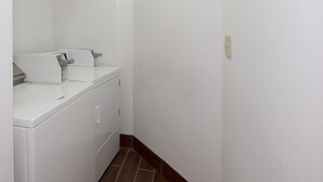 A narrow hallway with a washing machine and a dryer on the left, white walls, and a brown tiled floor. - Red Roof Inn Jackson, OH (Jackson)