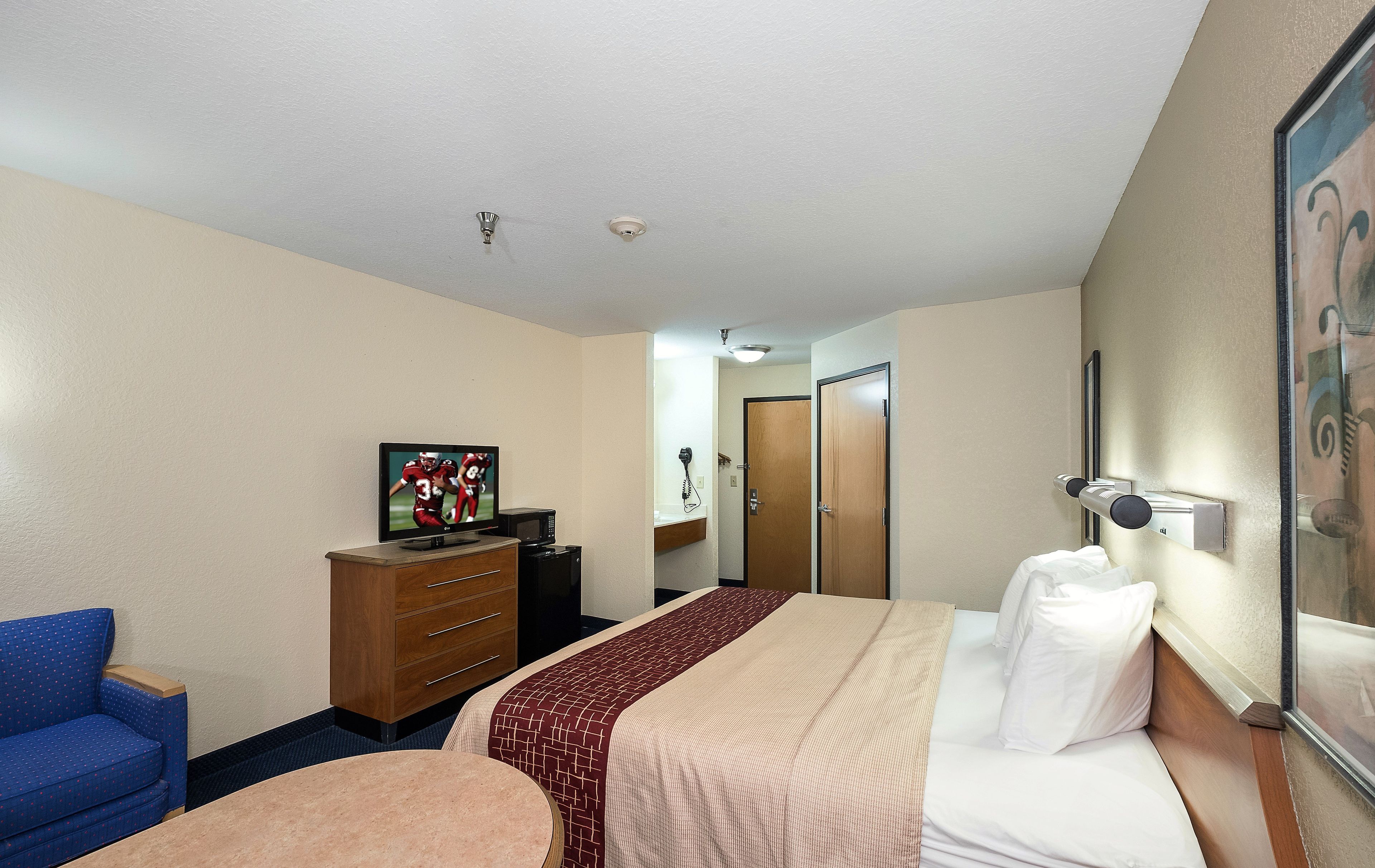 A hotel room with a bed, a TV, a dresser, a desk, and a chair.