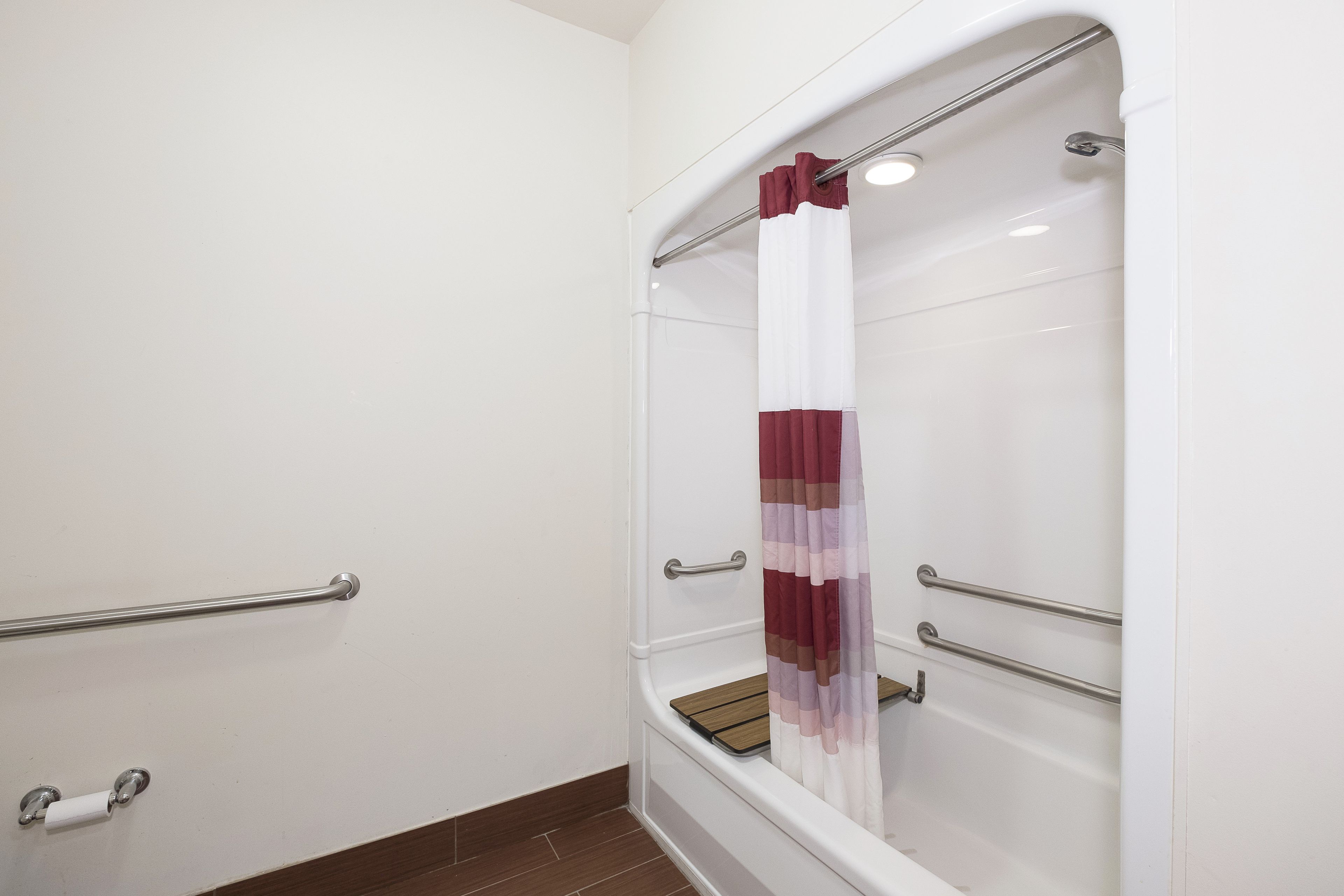 Une douche avec un mur recouvert de carreaux blancs, un sol en bois et un rideau de douche rayé de rouge et de blanc.