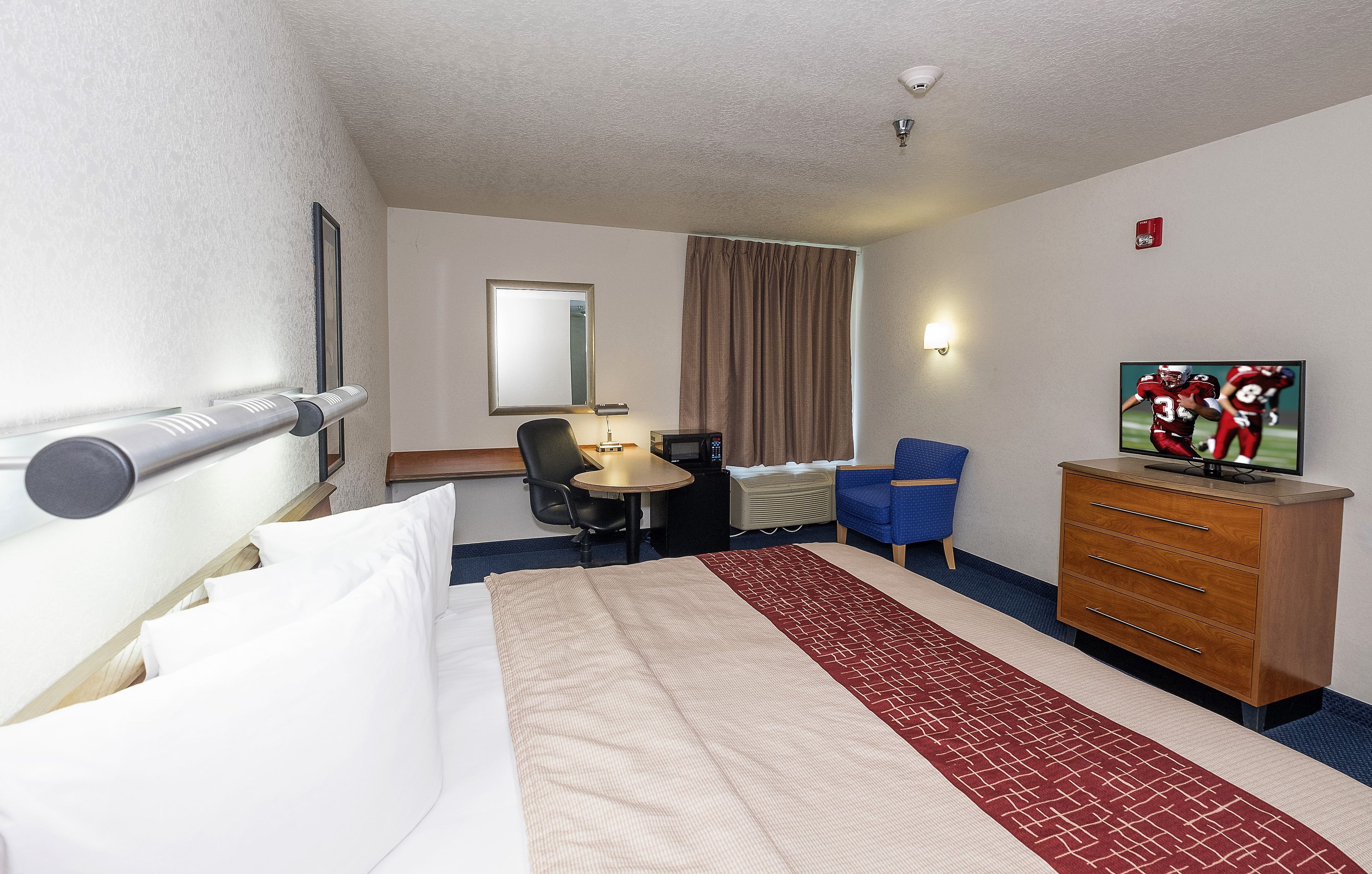 A hotel room with a bed, a desk, a chair, a television, and a dresser.