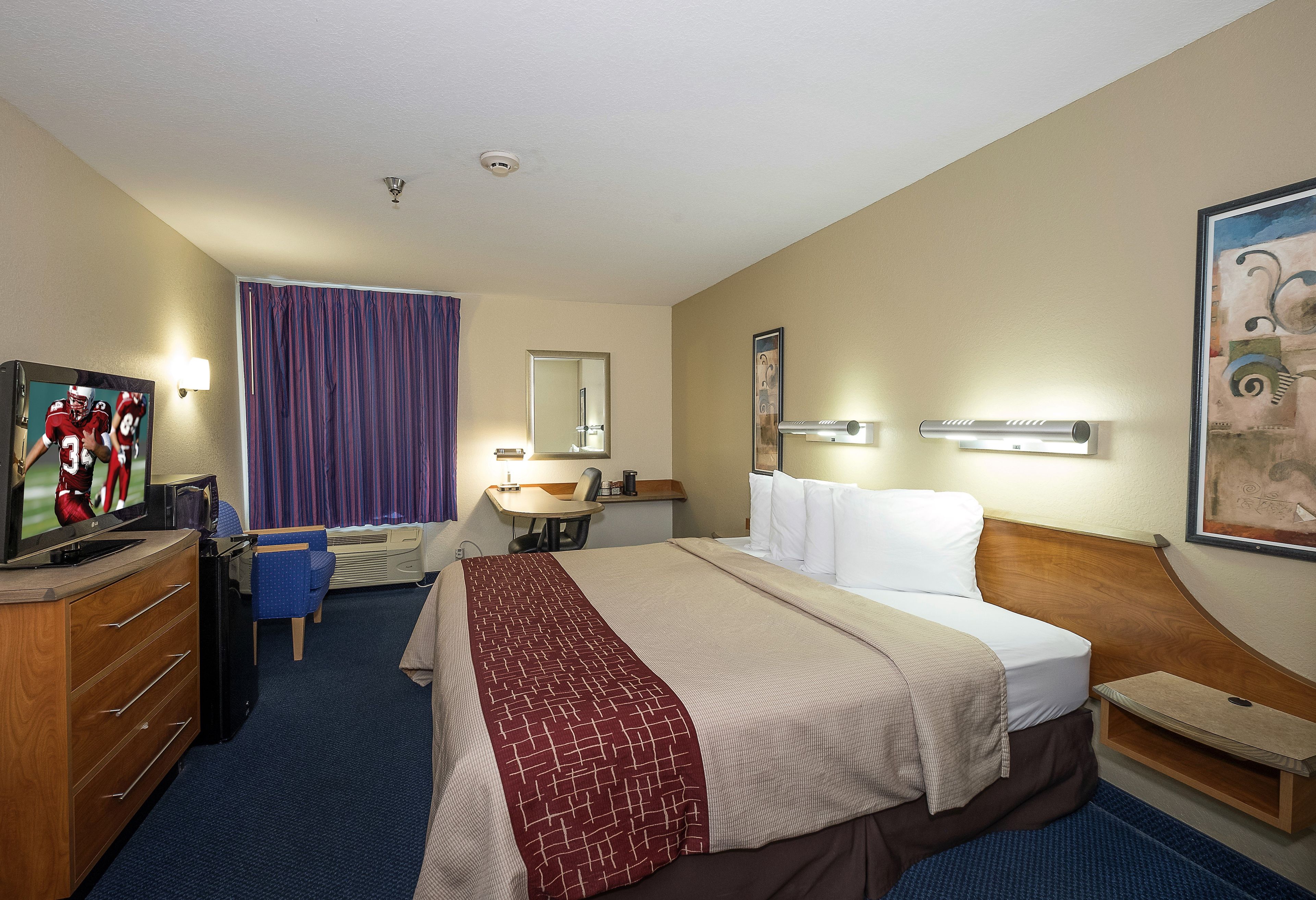A hotel room with a bed, a desk, a chair, a television, and a window with curtains.