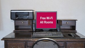 A desk with a printer, a monitor displaying 'Free Wi-Fi All Rooms,' a keyboard, a mouse, and a chair. - Red Roof Inn Jackson, OH (Jackson)