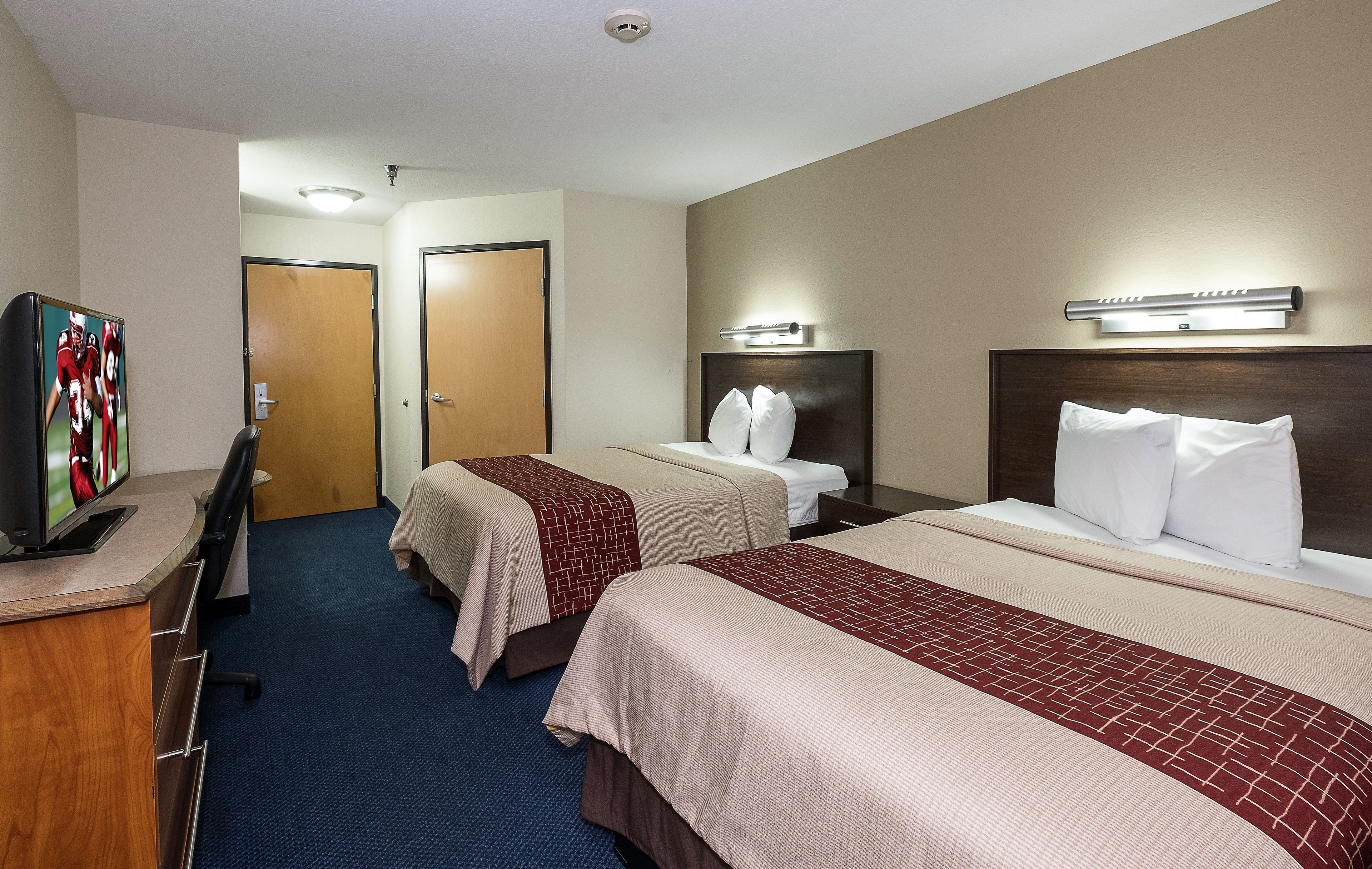 Ein Hotelzimmer mit zwei Betten, einem Fernseher und einem Schreibtisch.