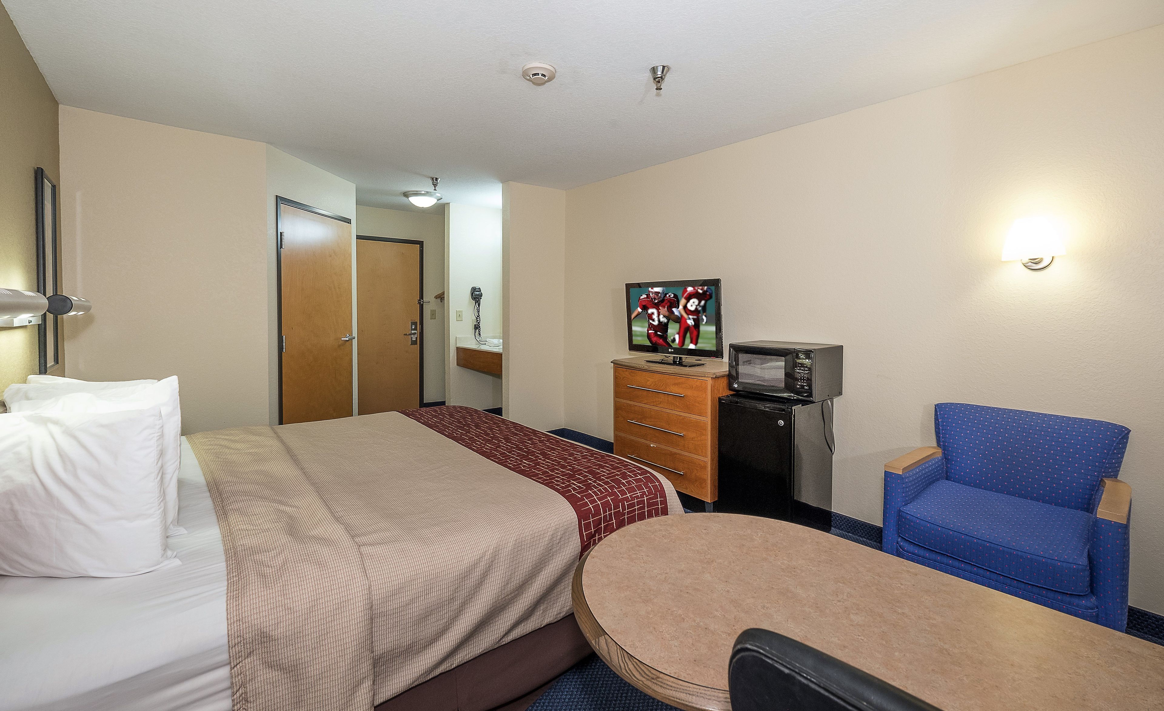 Une chambre d’hôtel équipée d’un lit, d’un bureau, d’une chaise, d’une commode, d’un four à micro-ondes et d’une télévision.