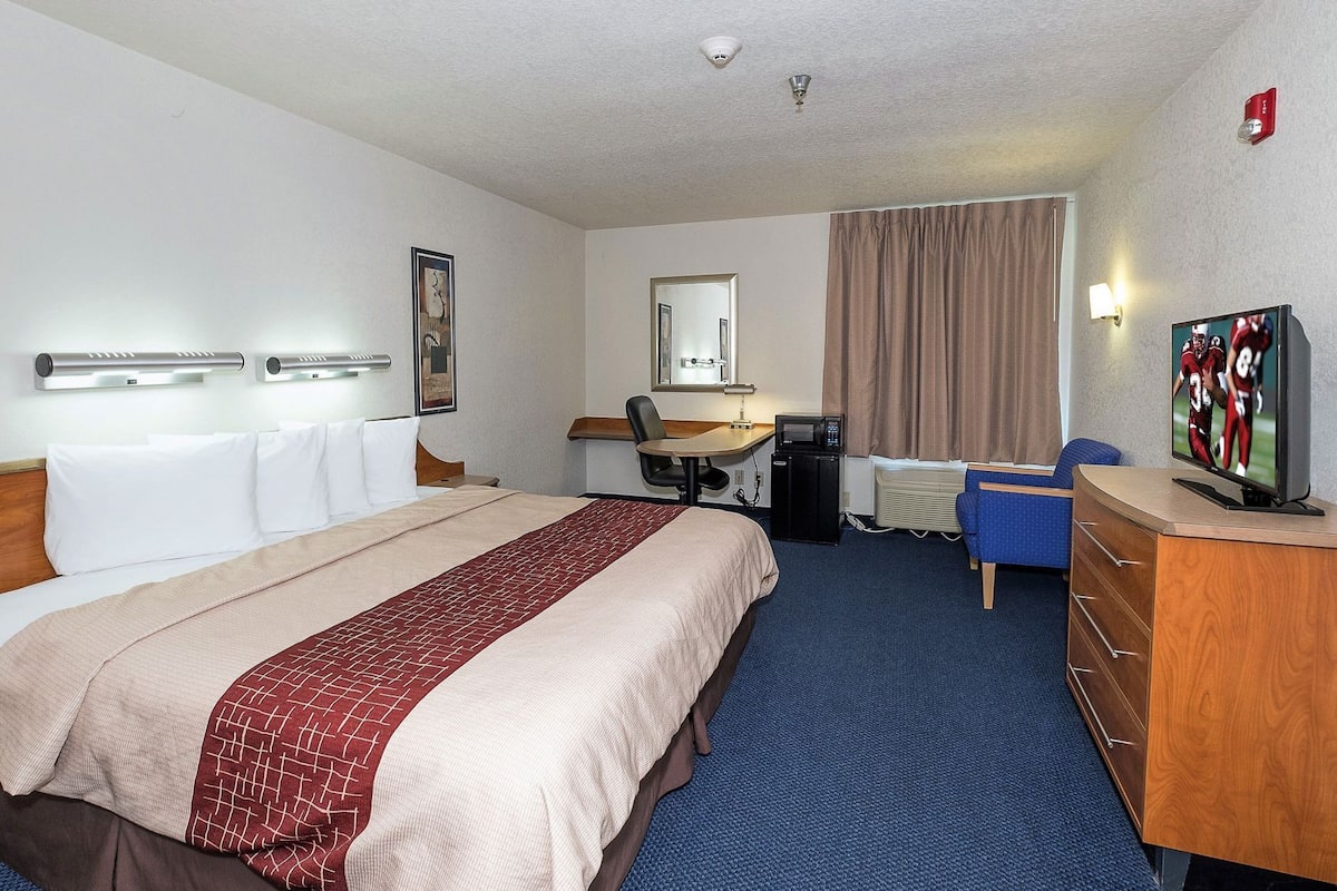 A hotel room with a bed, desk, chair, television, and a mirror.