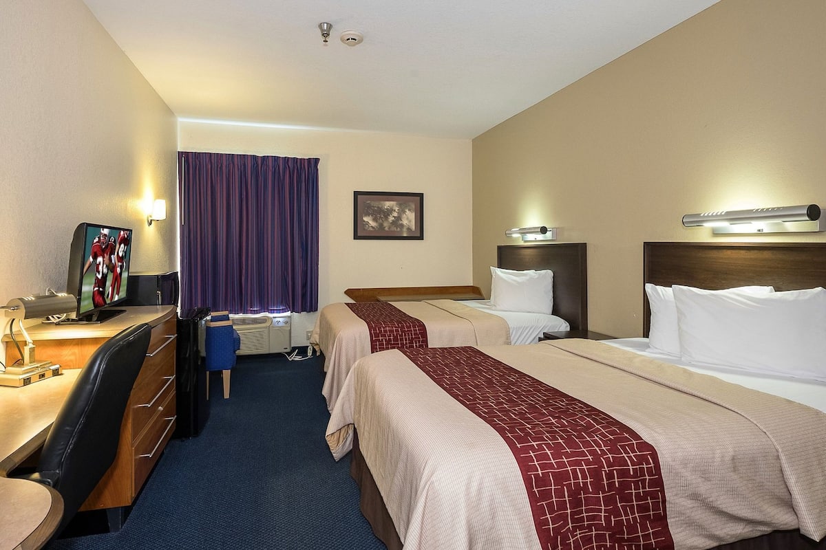 A hotel room with two beds, a desk with a computer, a chair, a TV, and a window with curtains.